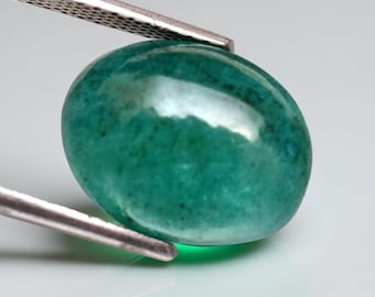 Pode incluir: Uma pedra preciosa oval polida, em tons de verde-azulado e verde, é segurada por uma pinça prateada. A gema tem uma superfície lisa e refletora, com um gradiente sutil de cor. A pedra preciosa é lapidada em cabochão.