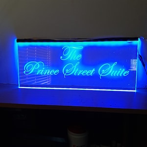 Peut inclure: Une enseigne LED bleue avec le texte "The Prince Street Suite" en &eacute;criture cursive blanche.