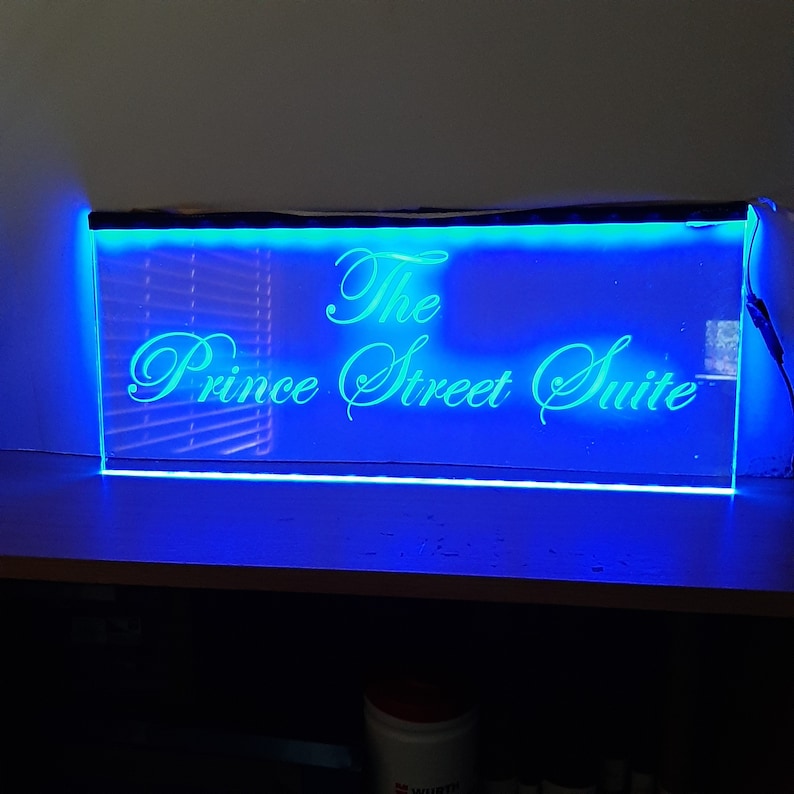 Peut inclure: Une enseigne LED bleue avec le texte "The Prince Street Suite" en &eacute;criture cursive blanche.