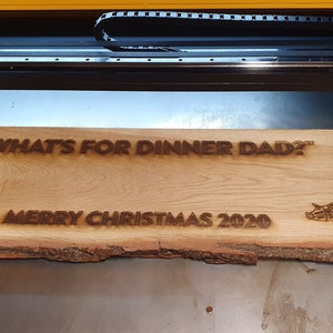 Peut inclure: Une pancarte en bois avec le texte "What's for dinner Dad?" et "Merry Christmas 2020" br&ucirc;l&eacute; &agrave; la surface. La pancarte pr&eacute;sente &eacute;galement une vache et un cochon avec des lignes de boucherie dessin&eacute;es dessus.