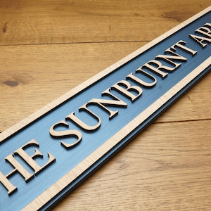 Peut inclure: Une enseigne en bois avec un fond bleu et des lettres blanches qui indiquent "The Sunburnt Arms".