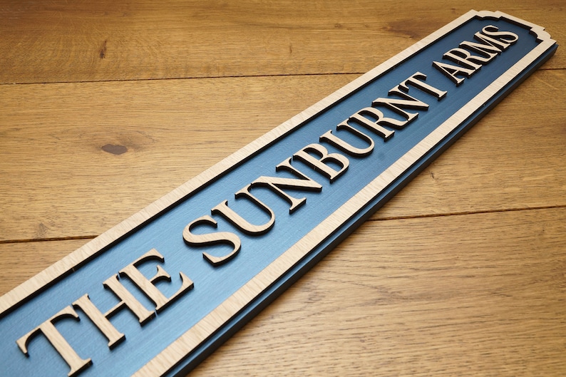 Peut inclure: Une enseigne en bois avec un fond bleu et des lettres blanches qui indiquent "The Sunburnt Arms".