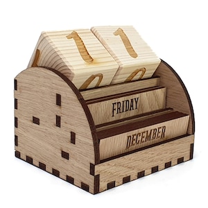 Peut inclure: Calendrier de bureau en bois avec une finition brun clair. Le calendrier pr&eacute;sente un design &agrave; rabat avec deux cubes pour la date, un affichage du jour de la semaine et un affichage du mois. Le calendrier est r&eacute;gl&eacute; sur le 1er d&eacute;cembre, vendredi.