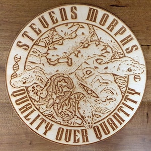 Peut inclure: Une enseigne ronde en bois avec une finition en bois brun. L'enseigne pr&eacute;sente un motif grav&eacute; au laser d&eacute;taill&eacute; de serpents entrelac&eacute;s avec le texte "Stevens Morphs" et "Quality Over Quantity".