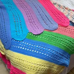 May include: A colorful crocheted blanket with stripes of blue, green, yellow, pink, and purple. The blanket is made with a variety of stitches and has a unique, handmade look.
