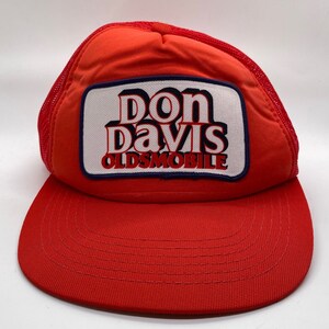 May include: Red and white mesh trucker hat with a white patch that says "Don Davis Oldsmobile" in a retro font.