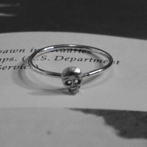 May include: A silver ring with a skull design. The ring is thin and delicate.