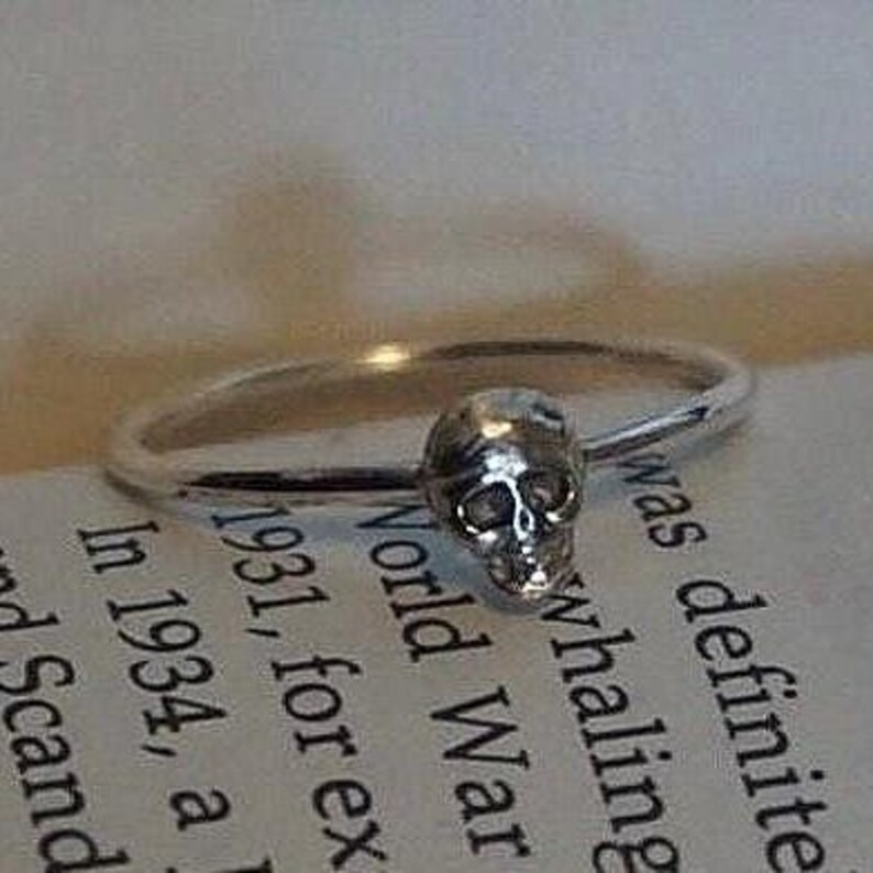 May include: A silver ring with a small skull charm. The ring is on a book with text about World War II.
