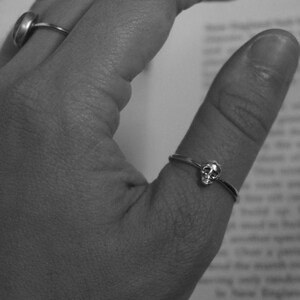 May include: A silver skull ring on a finger.