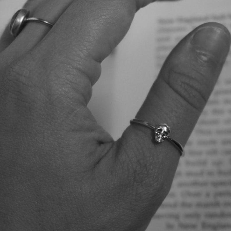 May include: A silver skull ring on a finger.