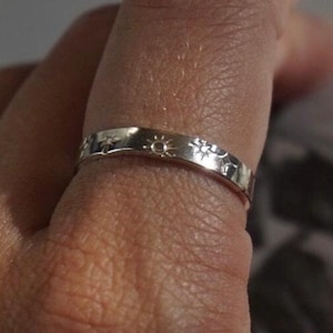 Puede incluir: Un anillo de plata con un diseño de sol y estrella. El anillo se lleva en un dedo.