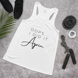 Könnte beinhalten: Ein weißes Tanktop mit dem Text "OOPS... I DID IT Again" in schwarzer Schrift. Das Tanktop liegt auf einer grauen Oberfläche mit einem Springseil und Gewichten.