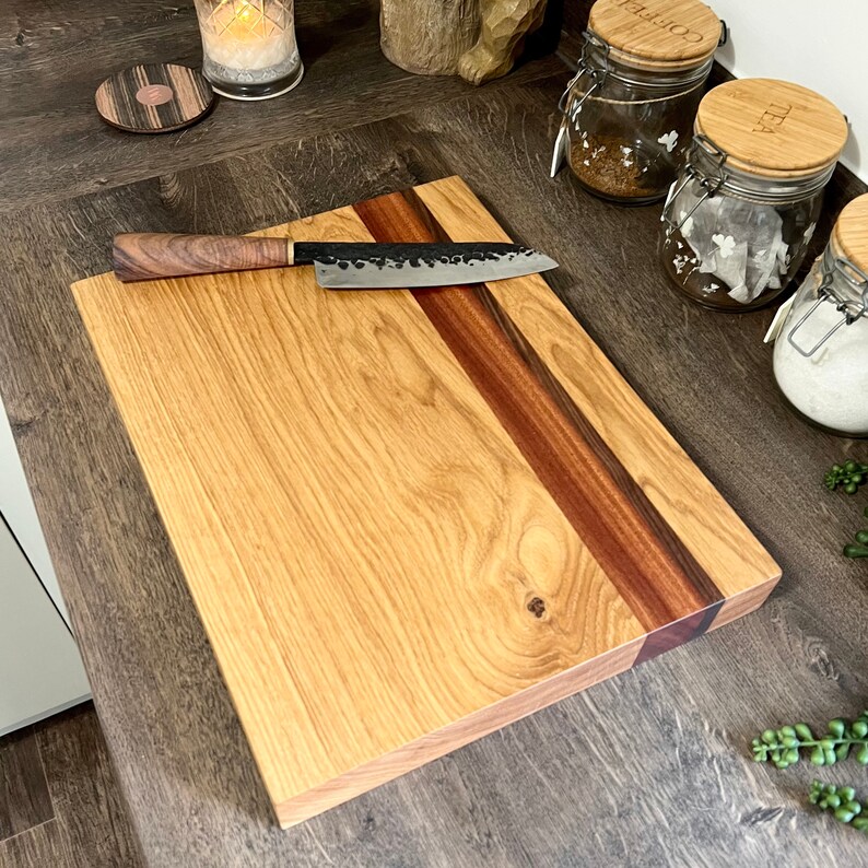 May include: A wooden cutting board with a dark wood stripe and a matching knife. The board is light brown with a dark brown stripe running diagonally across it. The knife has a dark metal blade and a wooden handle.
