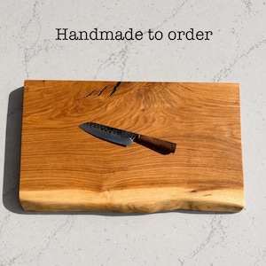 May include: A wooden chopping board with a live edge and a small knife. The board is light brown with darker wood grain patterns. The knife has a dark metal blade and a brown handle. Text on the image reads "Handmade to order."