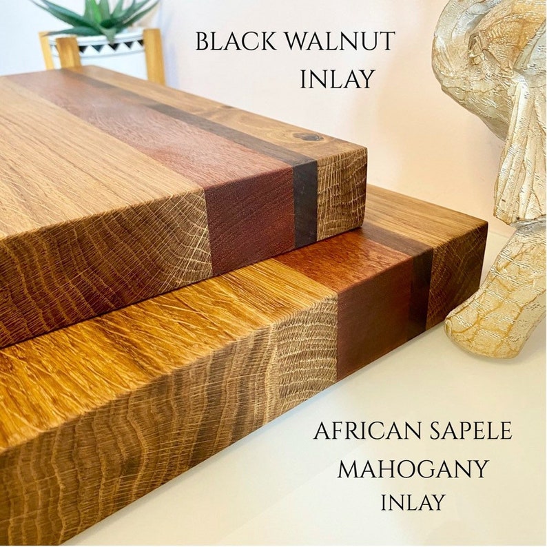 May include: Two wooden cutting boards with contrasting wood inlays. The top board features black walnut inlay, while the bottom board showcases African Sapele mahogany inlay. The boards are rectangular and have a natural wood grain.