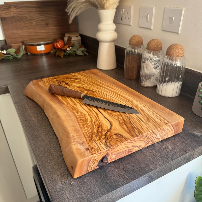 May include: A rectangular wooden cutting board with a live edge and a small knife. The board is made of light brown wood with a prominent grain pattern. The knife has a dark blade and a wooden handle. Kitchenware.