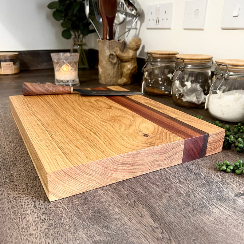 May include: A rectangular wooden cutting board with a light brown surface and a dark brown stripe. A matching knife with a wooden handle rests on the board. The board is made of hardwood and is suitable for kitchen use.