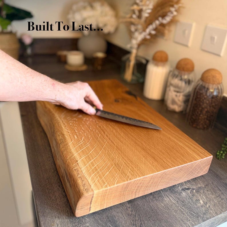 May include: A light brown wooden chopping board with a natural edge. A dark-handled knife rests on the board. The text "Built To Last..." is in the upper left corner. The board's dimensions are approximately 30 cm x 40 cm.