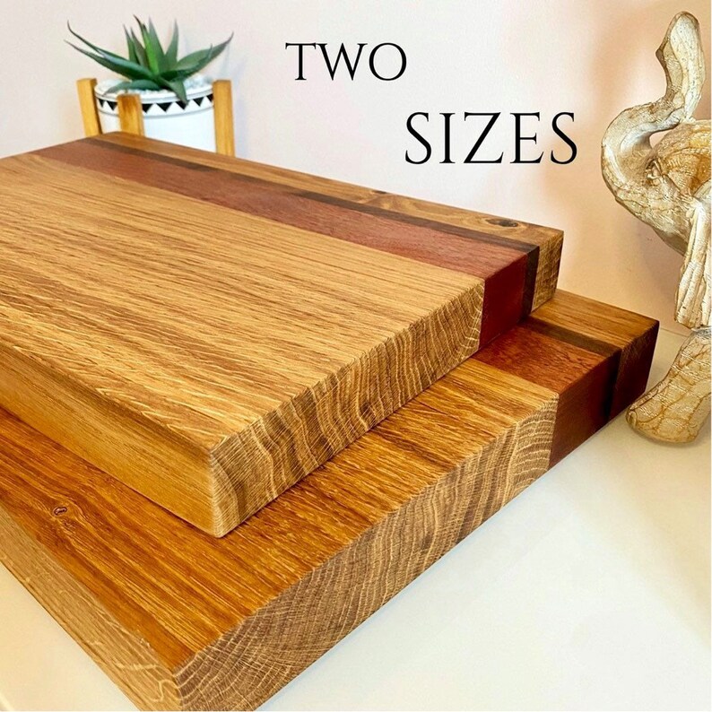 May include: Two wooden cutting boards in different sizes. The boards are made of light brown wood with a darker brown stripe. The text "TWO SIZES" is displayed in black.