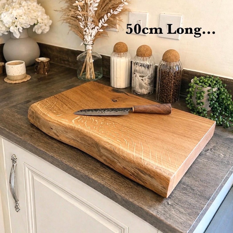 May include: A light brown wooden chopping board with a natural edge, measuring approximately 50cm long, with a knife on top. The board is on a countertop. The text "50cm Long..." is visible.