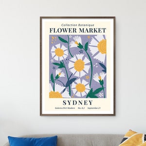 May include: A framed art print featuring a floral design with daisies in white and yellow against a lavender background. The print includes the text "Flower Market Sydney" and is displayed in a living room setting.