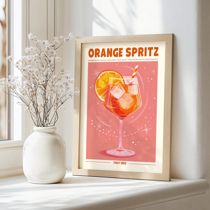 Puede incluir: Impresi&oacute;n enmarcada con una ilustraci&oacute;n del c&oacute;ctel Orange Spritz. La obra muestra una bebida naranja brillante con cubitos de hielo y una rodaja de naranja, sobre un fondo rosa. El texto "Orange Spritz" est&aacute; en la parte superior, con "Italy 1952" en la parte inferior.