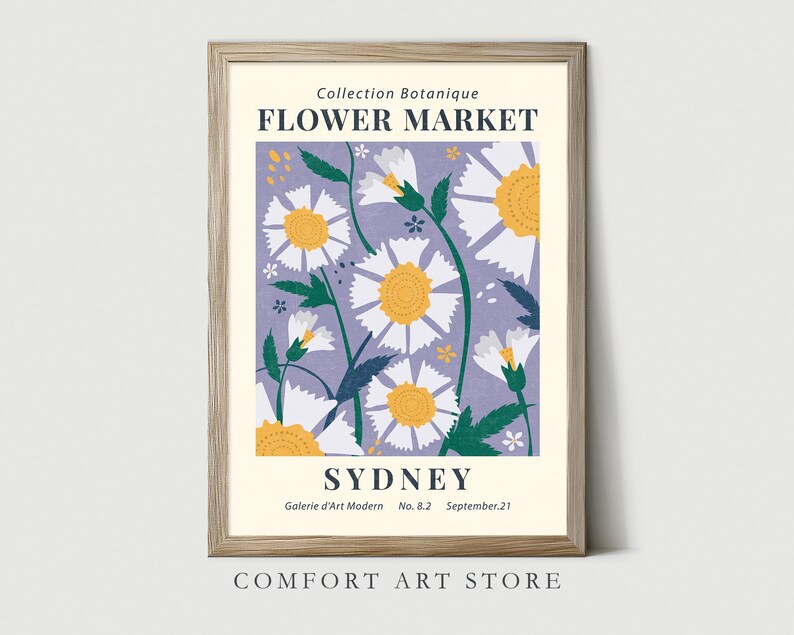 May include: A framed art print featuring a floral design with white and yellow daisies on a lavender background. The print includes the text "FLOWER MARKET SYDNEY" and "Collection Botanique". The frame is a light wood color.