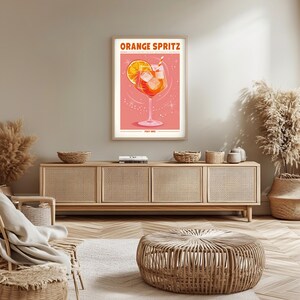 Puede incluir: Un p&oacute;ster enmarcado con las palabras "ORANGE SPRITZ" en naranja. El p&oacute;ster presenta una copa de c&oacute;ctel con una rodaja de naranja, cubitos de hielo y una pajita. El fondo es rosa con acentos en forma de estrella. El texto "ITALY 1919" est&aacute; en la parte inferior.