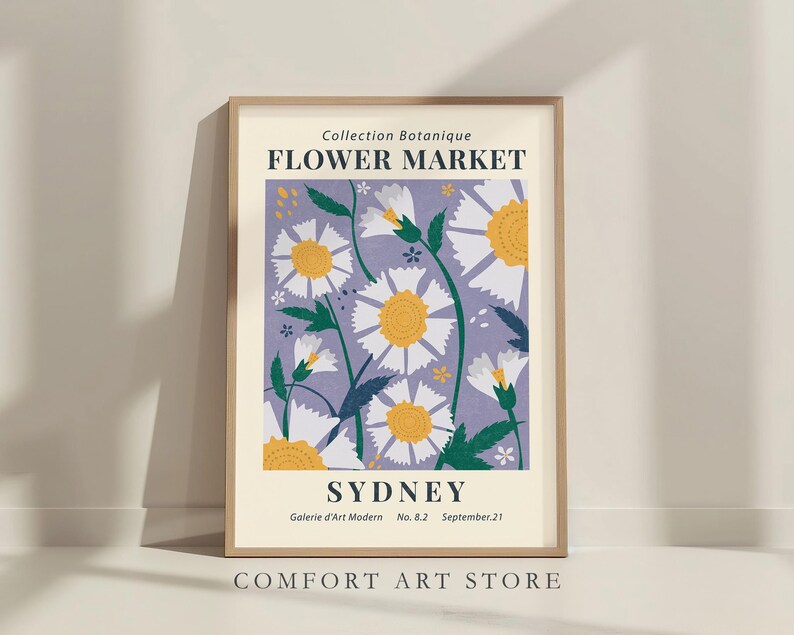 May include: A framed art print featuring a floral design with white and yellow daisies on a lavender background. The print includes the text "Flower Market Sydney" and "Comfort Art Store". The artwork is in a light wooden frame.