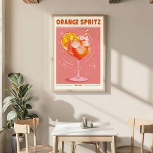 Puede incluir: Un p&oacute;ster enmarcado con las palabras "ORANGE SPRITZ" en la parte superior. El p&oacute;ster presenta una ilustraci&oacute;n estilizada de un c&oacute;ctel de naranja con cubitos de hielo y una pajita. El fondo es rosa claro con acentos en forma de estrella. El texto "ITALY 1952" est&aacute; en la parte inferior.