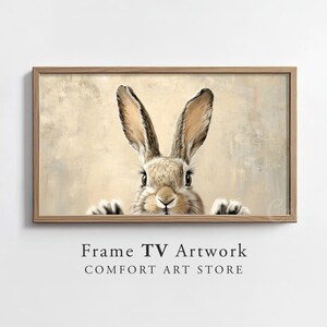 May include: A framed print of a brown rabbit with long ears peeking out from behind a beige background. The rabbit has a curious expression and its nose is twitching.