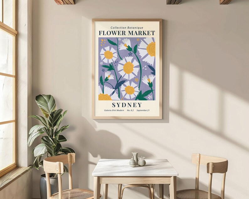May include: A framed poster with a floral design, featuring white daisies with yellow centers on a lavender background. The poster reads "FLOWER MARKET SYDNEY" in a vintage style. The poster is displayed in a room with a table and chairs.