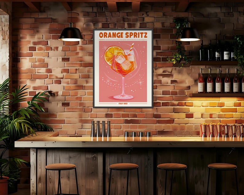 Puede incluir: Un p&oacute;ster enmarcado con las palabras "ORANGE SPRITZ" en la parte superior. El p&oacute;ster presenta un gr&aacute;fico de un c&oacute;ctel de naranja con cubitos de hielo y una pajita. El fondo es de color rosa claro. El p&oacute;ster est&aacute; colgado en una pared de ladrillo sobre una barra.