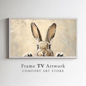 May include: A close-up of a brown rabbit with long ears peeking out from behind a textured beige background. The rabbit has a white nose and black eyes.