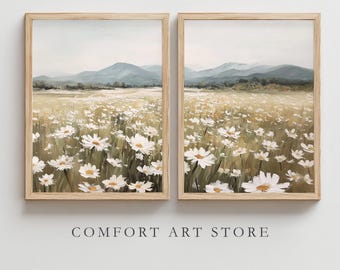 May include: Two framed landscape paintings depict a field of white daisies under a soft, overcast sky. Distant mountains are visible in the background. The frames are light-colored wood. The text "COMFORT ART STORE" is printed below the paintings.