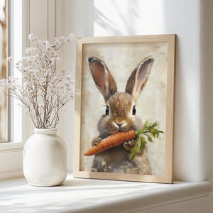 May include: A framed painting of a brown rabbit with long ears holding a carrot in its mouth. The rabbit is looking directly at the viewer. The background is a light beige color.
