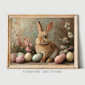 May include: A painting of a brown rabbit sitting amongst pastel pink and blue Easter eggs. The rabbit is surrounded by flowers and greenery. The painting is framed in a light wood frame.