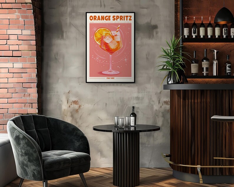 Puede incluir: Un p&oacute;ster enmarcado con las palabras "ORANGE SPRITZ" presenta una ilustraci&oacute;n de c&oacute;ctel con una rodaja de naranja y cubitos de hielo. El p&oacute;ster se exhibe en un ambiente de bar con una mesa negra, una silla de terciopelo y una estanter&iacute;a de licores.