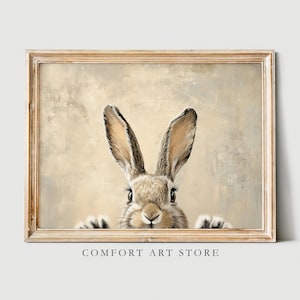 May include: A framed print of a rabbit peeking out from behind a beige background. The rabbit has brown fur and large ears.