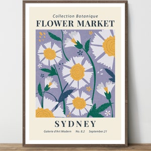May include: A framed art print featuring a floral design. The artwork showcases white daisies with yellow centers against a lavender background. Text includes "FLOWER MARKET" and "SYDNEY". The print is in a brown frame.