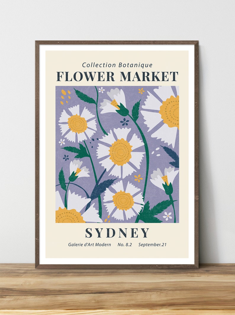 May include: A framed art print featuring a floral design. The artwork showcases white daisies with yellow centers against a lavender background. Text includes "FLOWER MARKET" and "SYDNEY". The print is in a brown frame.