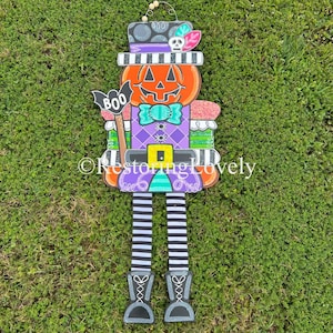 May include: A whimsical Halloween decoration featuring a pumpkin head with a top hat, bow tie, and striped legs. The pumpkin is orange with a carved face, and the outfit is purple and green. A bat with the word "BOO" is held in one hand. The boots are gray.