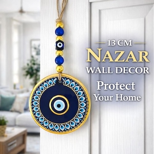 Op de afbeelding: Een blauw en goud Nazar wanddecoratie, 13 cm in diameter, met een boze oog ontwerp. De wanddecoratie heeft een gouden rand en een touwtje om op te hangen. De tekst op de afbeelding luidt "Nazar Wall Decor Protect Your Home."