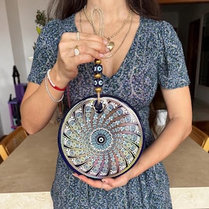 Peut inclure: Une décoration murale ronde bleu foncé avec un motif mandala coloré et détaillé. Le mandala présente des motifs complexes dans des tons de bleu, blanc, jaune et rose. Il possède une boucle de suspension en corde et perles.