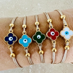 Può includere: Cinque braccialetti regolabili con una catena dorata e un ciondolo a forma di trifoglio con un design di occhio turco. I ciondoli sono di diversi colori: blu, turchese, verde, rosso e bianco.