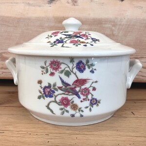 May include: White ceramic serving dish with a lid, featuring a colorful floral and bird design. The dish has two handles and a knob on the lid. The design includes pink, blue, and green flowers and birds on a white background.