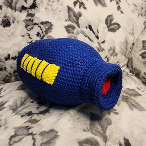 May include: Blue crocheted plush toy shaped like a missile with yellow and red details.