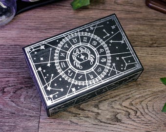 Puede incluir: Caja negra con un diseño plateado de una rueda zodiacal con la constelación de Cáncer. La caja tiene un borde plateado y un fondo negro.