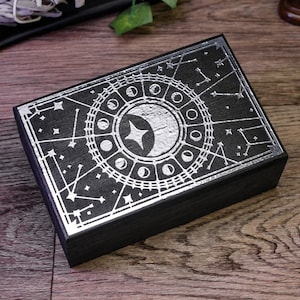 May include: A black wooden box with a silver design of a moon and stars. The box has a hinged lid and is ideal for storing small items.