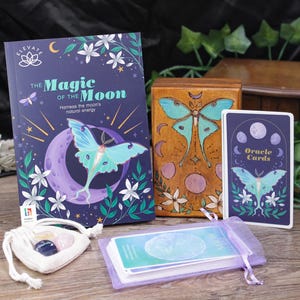May include: A set of moon oracle cards with a wooden box, a book titled "The Magic of the Moon", and a small pouch with crystals. The cards feature a blue and purple moth design with a crescent moon.